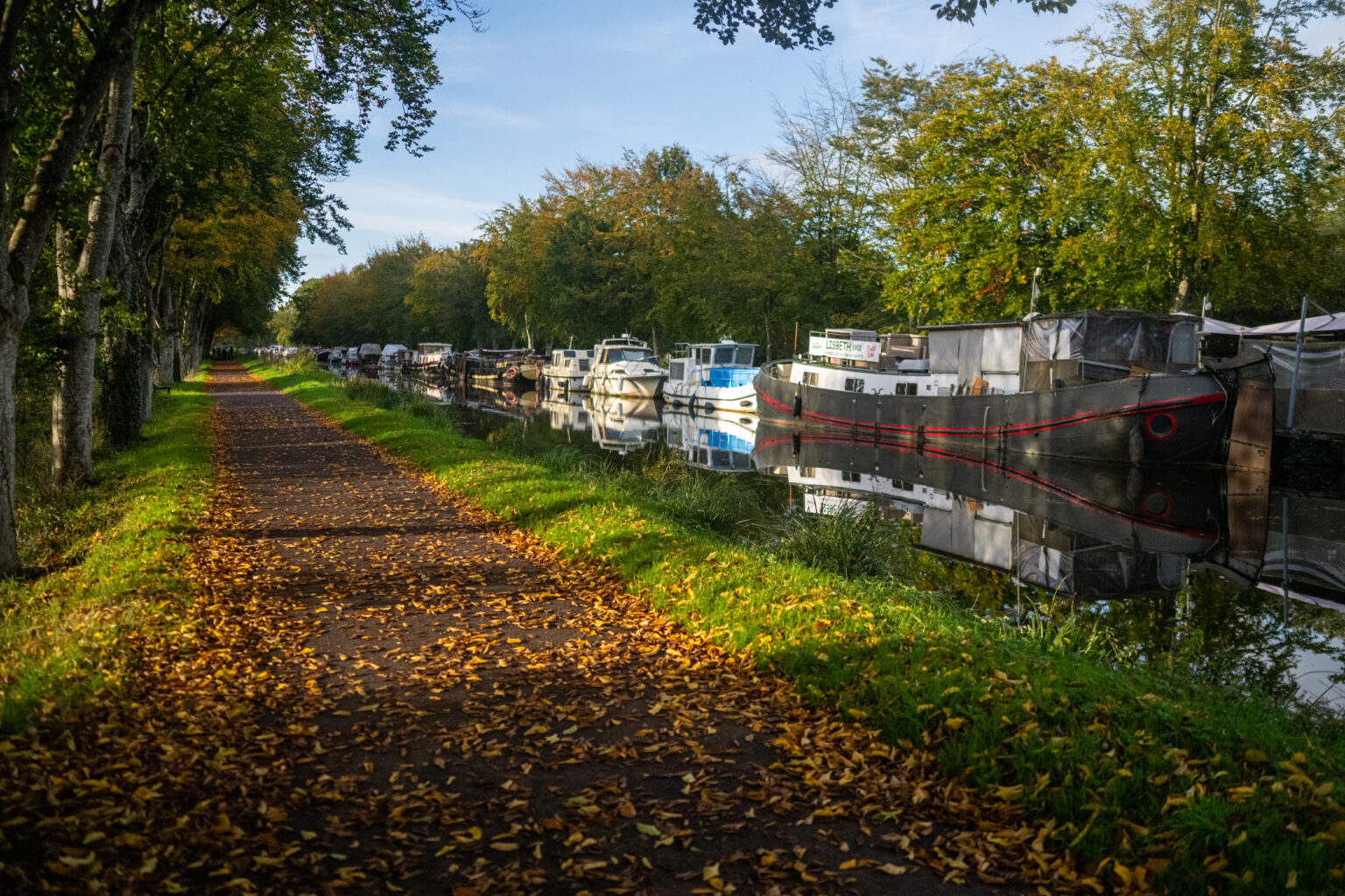 Chemin de halage bordé d’arbres et bateaux amarrés le long du canal à Malestroit